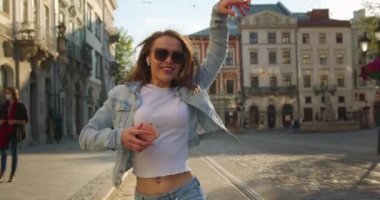 Güneş gözlüklü neşeli bir kız şarkı söylüyor ve dans ediyor. O gülüyor ve küçük kulaklıklarla müzik dinliyor. Saçları rüzgarda dalgalanıyor. 4K