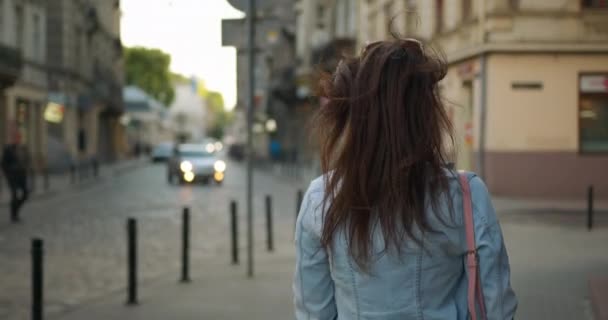 Schießen von hinten. Ein Mädchen läuft die Straße hinunter. Ihre Haare fliegen im Wind. Sie dreht sich um und gestikuliert mit der Hand, um ihr zu folgen. 4k — Stockvideo