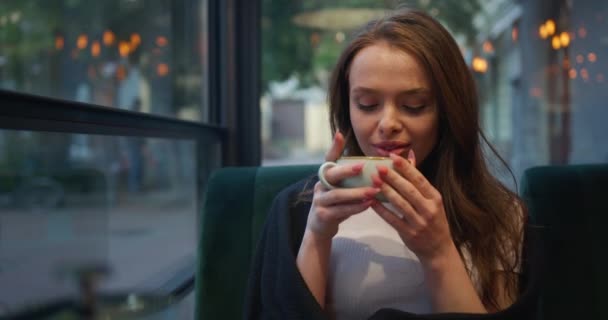 Disparos de cerca. La chica está sentada en un café en la terraza. Ella está bebiendo té y disfrutando del ambiente. La chica está envuelta en una manta. 4K — Vídeos de Stock