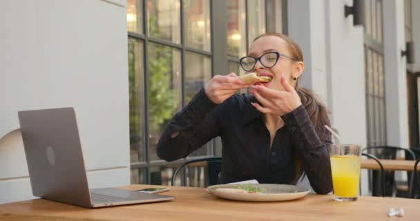 Dziewczyna je pizzę i pije lemoniadę. Smakuje jej lunch. Bizneswoman pracuje na werandzie kawiarni. Nosi okulary i koszulę. 4K — Wideo stockowe