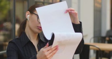 Yakın plan çekim. İş kadını çalışan belgelere dikkatlice bakıyor. Bilgiyi görmek için gözlüklerini indiriyor. O, bir kafede bir masada oturuyor. Masanın üzerinde.