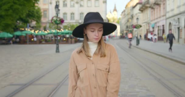 La cámara está acercándose a la chica. La chica está de pie y mirando a la cámara. Su cabello vuela en el viento y ella sonríe. Lleva un gran sombrero negro. 4K — Vídeo de stock