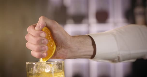 Sparatoria ravvicinata. Un barista sta spremendo l'arancia nel bicchiere durante la preparazione del cocktail. 4k — Video Stock