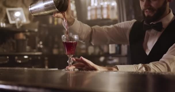 Disparos de cerca. El camarero está vertiendo el alcohol de la coctelera a través de un colador de cóctel en el vaso. 4k — Vídeo de stock