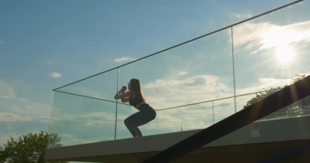 那个女体育运动员正在做蹲式跳伞动作.她跳的时候，头发在飘扬。她戴太阳镜。拍摄从底部顺利通过相机。4K — 图库视频影像
