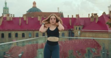 Sportif bir kız kameraya bakıyor ve saçını düzeltiyor. O, cam korkuluklara yaslanıyor. Kız spor üniforması ve pembe gözlük takıyor. Kamera ona doğru yavaşlıyor. 4K