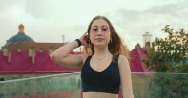 Sportif bir kız gidiyor ve saçını düzeltiyor. O, kameraya bakıyor. Kamera sorunsuzca uzaklaşıyor. Kız spor üniforması ve pembe gözlük takıyor. Yakın plan çekim. 4K