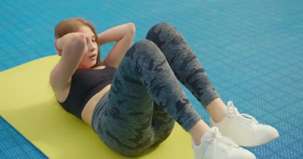 Крупный план. Девушка трясет пресс, выполняя велосипедные упражнения. Девушка одета в спортивную форму. Она лежит на коврике для йоги. 4K — стоковое видео
