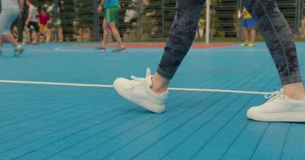 Närbild av en flickas ben. En tjej går på en basketplan. Folk spelar hockey i bakgrunden. 4K — Stockvideo