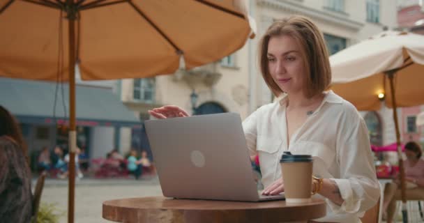 Fata stă pe verandă într-o cafenea. Lucrează la laptopul ei. Își închide laptopul când termină și lasă un suspin de ușurare. Există o ceașcă de cafea pe masă — Videoclip de stoc