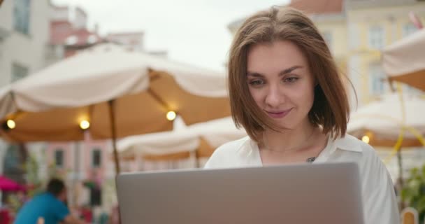 Tiroteio de perto. A menina está sentada em um café e trabalhando em um laptop. As pessoas andam ao fundo. 4K — Vídeo de Stock