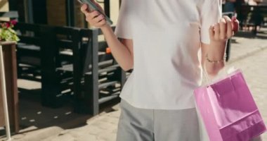 Bir kız şehirde yürüyor ve akıllı telefonuyla mesaj atıyor. Kolunda alışveriş torbaları asılı. O bir şapka ve güneş gözlüğü takıyor. 4K