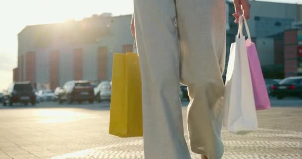 Kız otoparkta yavaşça yürüyor. O, alışveriş torbaları taşıyor. Arka plandaki alışveriş merkezi. 4K — Stok video