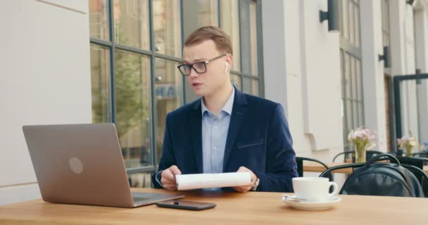 Un hombre de negocios está discutiendo indignado cuestiones de negocios en una reunión a través de una videollamada en un ordenador portátil. Él está sentado en un café y en la mesa una taza de té. 4K — Vídeos de Stock