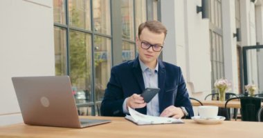 Bir iş adamı bir kafede oturuyor ve çalışıyor. Aynı anda hem telefona cevap veriyor hem de çay içiyor. Masada bir dizüstü bilgisayar var. 4K