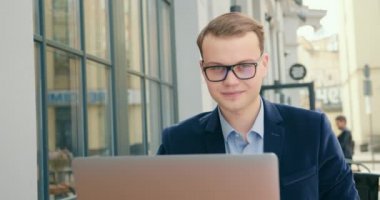 Bir iş adamı bir kafede oturuyor ve çalışıyor. Kameraya bakıyor ve 