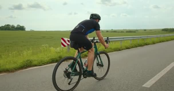 El ciclista está conduciendo rápidamente la carretera y cambiando la transmisión. Entrenamiento en bicicleta. Hay un campo verde en el fondo. 4K — Vídeos de Stock