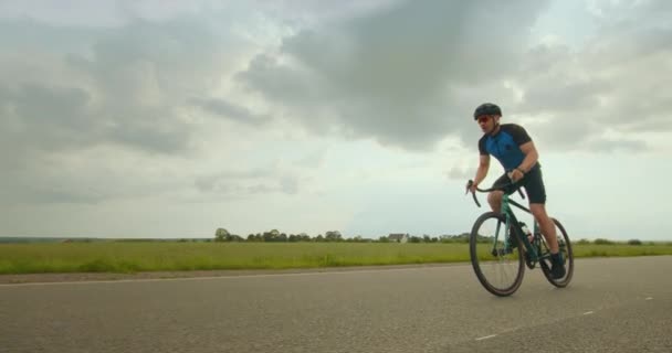 Rowerzysta jedzie wzdłuż autostrady i zwiększa prędkość. Jedzie pod górę. Trening na rowerze. Pola w tle. 4K — Wideo stockowe