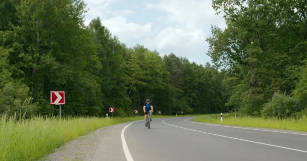 Un ciclista está montando en la carretera. Entrenamiento en bicicleta. Bosque en el fondo. 4K — Vídeos de Stock