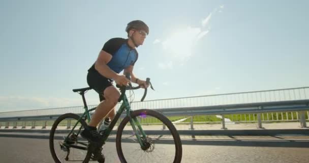 Bisikletli bir sporcu pedalların üzerinde duruyor ve büyük bir hız kazanıyor. Bisiklet üstünde antrenman. Arka planda güneş var. 4K — Stok video