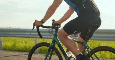 Bisikletli bir sporcu otoyol boyunca sürüyor. Bisikletçilerin bacaklarına yakın çekim. Bisiklet üstünde antrenman. 4K