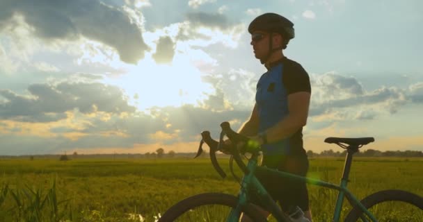 En idrottsman går längs vägen med en cykel. Han tittar på sin fitness tracker. Träning på cykel. Solnedgång i bakgrunden. 4k — Stockvideo