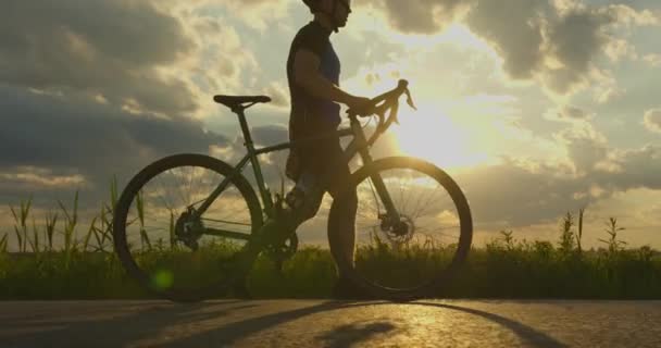 Sportowiec spaceruje po drodze z rowerem. Trening na rowerze. Zachód słońca w tle. 4k — Wideo stockowe
