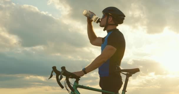 自転車は道路の端に立っており、背景のボトルサンセットから水を飲んでいます。クローズアップ撮影。4K — ストック動画