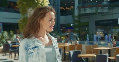 Bir kız alışveriş merkezinde yürüyor. Arkadaki kafeler ve dükkanlar. Yakın plan çekim. 4K