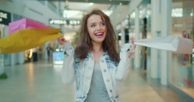 Kız mutlu ve gülümsüyor. O, alışveriş torbalarını omzunun üzerinden atıyor. Mağazalar arka planda. 4K