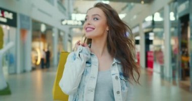 Kız gülümsüyor ve alışveriş merkezinde yürüyor. O, alışveriş torbalarını omzunun üzerinden atıyor. 4K