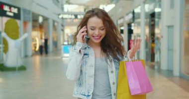 Kız telefonda duygusal konuşuyor ve alışveriş merkezinde dolanıp duruyor. O, elinde alışveriş torbaları tutuyor. 4K