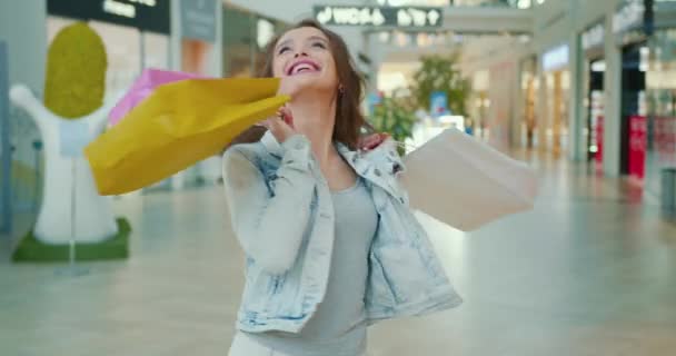 女の子は幸せと好転しています。彼女は買い物袋を手に持っている。背景に店舗。4K — ストック動画