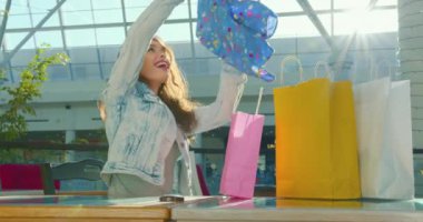 Kız bir masada oturuyor ve satın aldıklarına bakıyor. Bluzunu çantasından çıkarmaktan mutluluk duyuyor. 4K