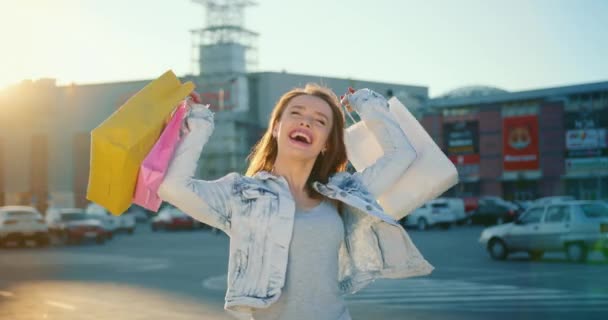 Das Mädchen lächelt und ist glücklich. Sie hält die Einkaufstüten hoch. Im Hintergrund ein Einkaufszentrum. 4K