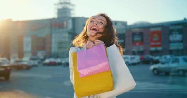 Das Mädchen lächelt. Sie hält Einkaufstüten in den Händen. Sie steht auf dem Parkplatz des Einkaufszentrums. Im Hintergrund scheint die Sonne. 4K