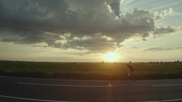 Un ciclista está montando rápido en la carretera. Puesta de sol en el fondo. Disparando desde un dron. 4K — Vídeos de Stock