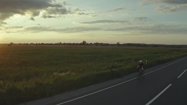 Rowerzysta jedzie szybko po autostradzie. Zachód słońca w tle. Dron krąży wokół niego. 4K — Wideo stockowe