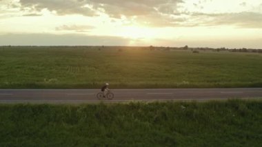 Bir sporcu bisiklete biniyor. Arka planda gün batımı. Bir İHA 'dan ateş etmek. 4K