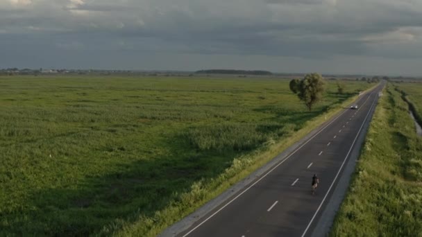 Un ciclista sta passando rapidamente lungo l'autostrada. Sparo da un drone. Allenamento in bicicletta. Le auto gli passano accanto. 4K — Video Stock