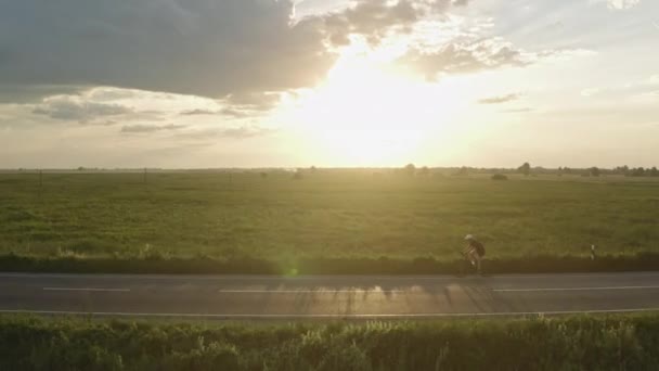 Sportowiec szybko jeździ na rowerze. Jeździ na poboczu autostrady. Trening na rowerze. Dron krąży wokół niego. 4K — Wideo stockowe