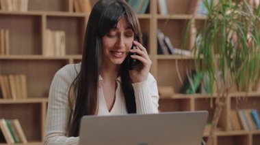 Gülümseyen beyaz bir kadın elinde telefonla neşeli sohbetin tadını çıkarıyor. Uzaktaki iş sırasında birden fazla iş yaparken ve neşeli bir ruh hali içindeyken iş arkadaşınla ya da arkadaşınla konuşmak.