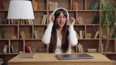 Beyaz kulaklık takan beyaz kadın müzikten hoşlanıyor. Kapalı dizüstü bilgisayarla masada oturmak. İki elinle kulaklığı tut. Gözler kapalı. Şarkının derin duygusal bağlantısını gösteriyor.