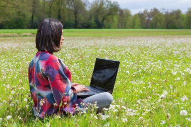 Arazide beyaz çiçekli laptop ile oturan kadın