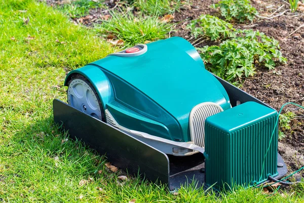 Green electric robotic Lawnmower charging on grass