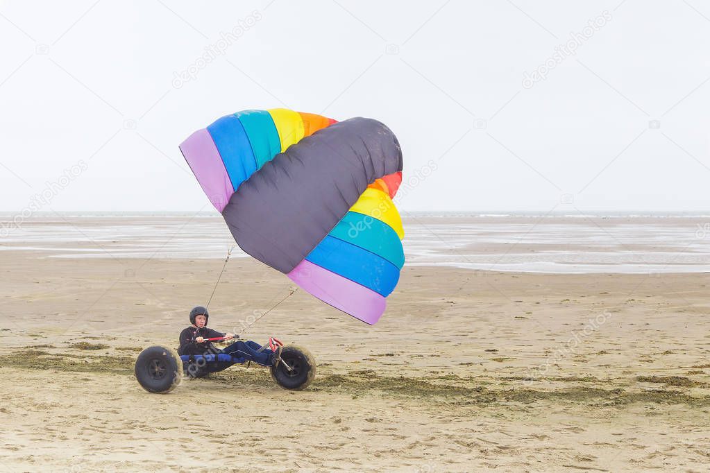 Caucasian male teen drivesg kite buggy with kite flyer on beach with sea