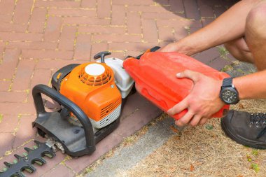 Male gardener filling hedge trimmer with fuel clipart