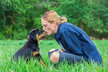 Genç beyaz dişi köpek sahibi üzerinde doğal çayır kafasından rottweiler yavrusu kisses