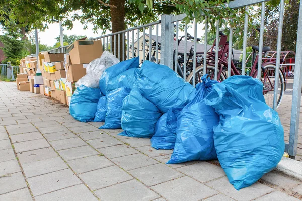 Blue garbage bags and boxes with waste are standing on dutch footpath