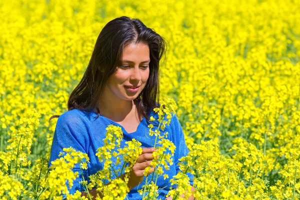 Mujer mira la flor en el campo de colza amarillo — Foto de Stock